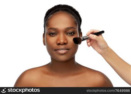 beauty, cosmetics and people concept - portrait of face of beautiful young african american woman and hand with make up brush applying blush to skin over white background. african woman and hand with make up brush