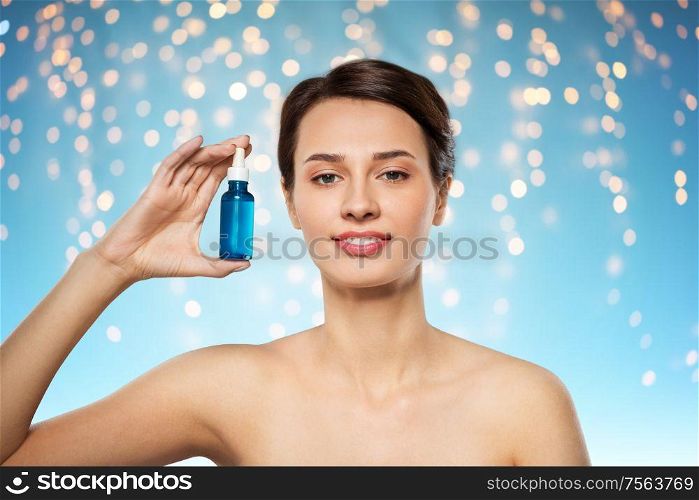 beauty, cosmetics and skincare concept - happy young woman with bottle of serum over holidays lights on blue background. beautiful young woman with bottle of serum