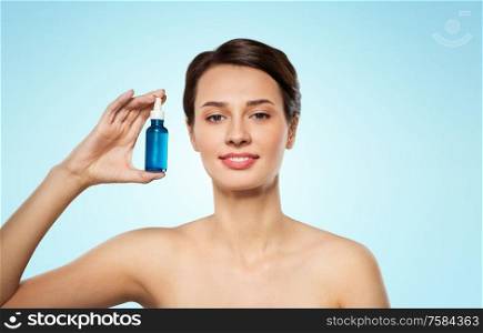 beauty, cosmetics and skincare concept - happy young woman with bottle of serum over blue background. beautiful young woman with bottle of serum
