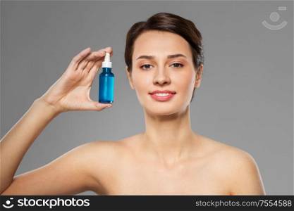 beauty, cosmetics and skincare concept - happy young woman with bottle of serum over grey background. beautiful young woman with bottle of serum