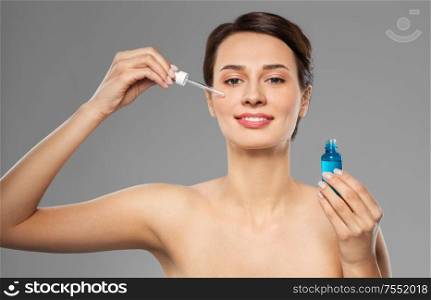 beauty, cosmetics and skincare concept - happy young woman with dropper applying serum to her face over grey background. woman with dropper applying serum to her face
