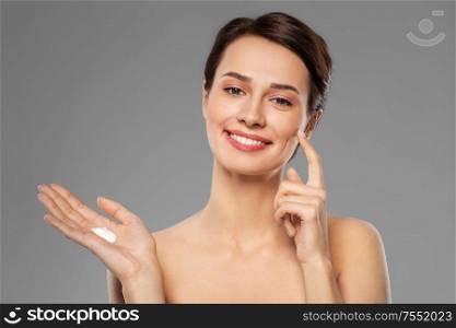 beauty, cosmetics and skincare concept - happy young woman with moisturizing cream on finger over grey background. young woman with moisturizing cream on finger