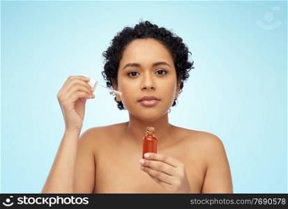 beauty, cosmetics and skincare concept - portrait of young african american woman with bare shoulders holding bottle of serum or face oil over blue background. african american woman with bottle of serum