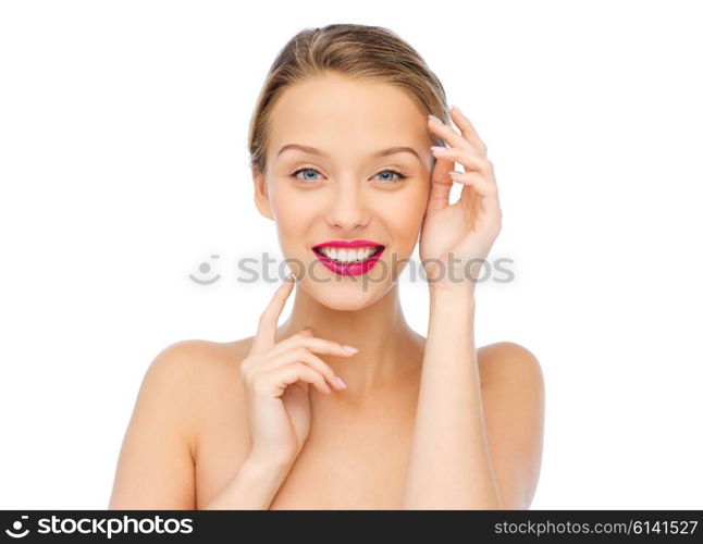 beauty, cosmetics, people and health concept - smiling young woman with pink lipstick on lips touching her face