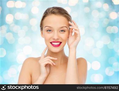 beauty, cosmetics, people and health concept - smiling young woman with pink lipstick on lips touching her face over blue holidays lights background