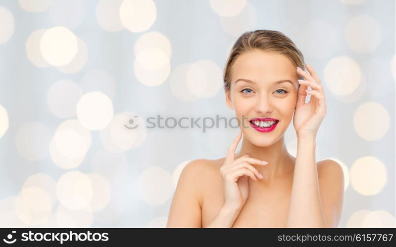 beauty, cosmetics, people and health concept - smiling young woman with pink lipstick on lips touching her face over holidays lights background