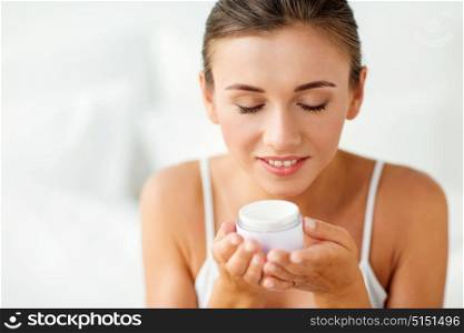 beauty, cosmetics, skin care and people concept - close up of beautiful happy woman holding and smelling cream jar. close up of happy woman holding and smelling cream
