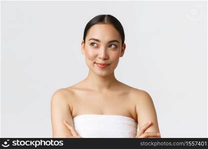 Beauty, cosmetology and spa salon concept. Close-up of confident and pleased smiling gorgeous asian woman, wearing bath towel and smiling as looking left, having idea, white background.. Beauty, cosmetology and spa salon concept. Close-up of confident and pleased smiling gorgeous asian woman, wearing bath towel and smiling as looking left, having idea, white background