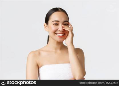 Beauty, cosmetology and spa salon concept. Close-up of gorgeous asian woman in bath towel laughing and smiling white teeth, gently touching face, clean skin and skincare concept.. Beauty, cosmetology and spa salon concept. Close-up of gorgeous asian woman in bath towel laughing and smiling white teeth, gently touching face, clean skin and skincare concept