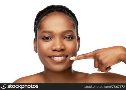 beauty, dental care and people concept - beautiful smiling young african american woman pointing to her mouth over white background. african american woman pointing to her mouth