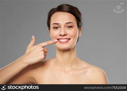beauty, dental care and people concept - beautiful smiling young woman pointing to her mouth or teeth over grey background. smiling young woman pointing to her mouth