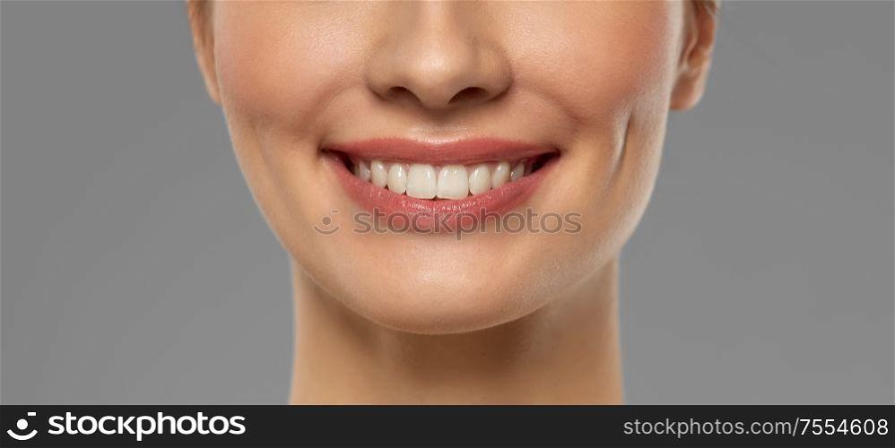 beauty, dental care and teeth whitening concept - close up of beautiful young woman with white smile over grey background. close up of beautiful young woman with white smile