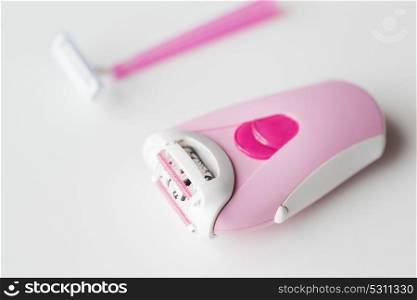 beauty, depilation and hair removal concept - close up of epilator and safety razor on white background. epilator and safety razor on white background