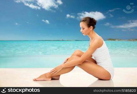 beauty, depilation, epilation, people and bodycare concept - beautiful woman touching her smooth bare legs over exotic tropical beach background. beautiful woman touching her smooth legs on beach