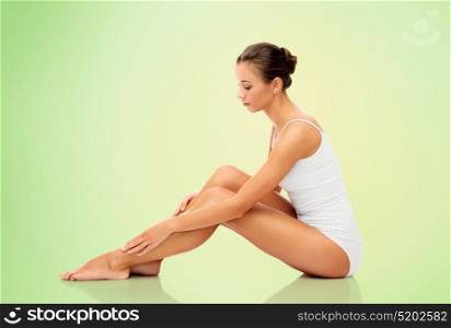 beauty, depilation, epilation, people and bodycare concept - beautiful woman touching her smooth bare legs over green background. beautiful woman touching her smooth bare legs