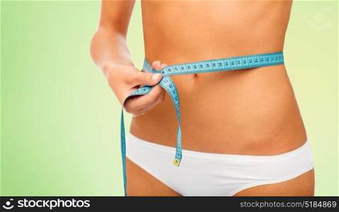 beauty, diet, weight loss and people concept - close up of slimming woman body with measure tape around waist over green background. close up of woman body with measure tape on waist