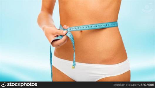 beauty, diet, weight loss and people concept - close up of slimming woman body with measure tape around waist over blue background. close up of woman body with measure tape on waist