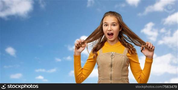 beauty, emotions and people concept - stressed or scared young teenage girl holding her hair strands over blue sky and clouds background. scared young teenage girl holding her hair strands