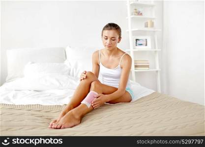 beauty, epilation, hair removal and people concept - beautiful woman applying depilatory wax strip to her leg skin at home bedroom. woman removing leg hair with depilatory wax strip