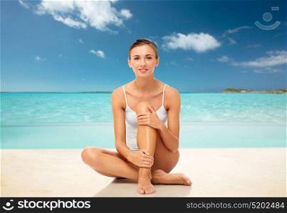 beauty, epilation, people and bodycare concept - beautiful woman touching her smooth bare legs over exotic tropical beach background. beautiful woman touching her smooth legs on beach
