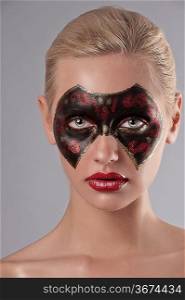 beauty face shot of a young woman having a black and red carnival mask painted on her face