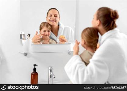 beauty, family and people concept - happy smiling mother and daughter with moisturizer in bathroom. mother and daughter with moisturizer in bathroom