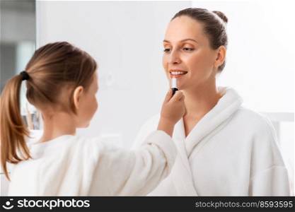 beauty, family and people concept - happy smiling mother and little daughter with lipstick applying make up in bathroom. mother and daughter applying make up in bathroom
