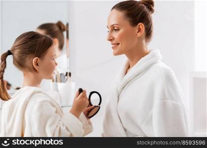 beauty, family and people concept - happy smiling mother and little daughter with brush and powder applying make up in bathroom. mother and daughter applying make up in bathroom