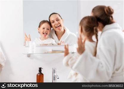 beauty, family and people concept - happy smiling mother and little daughter looking to mirror and hugging in bathroom. mother and daughter looking to mirror in bathroom
