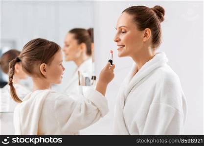 beauty, family and people concept - happy smiling mother and little daughter with lipstick applying make up in bathroom. mother and daughter applying make up in bathroom