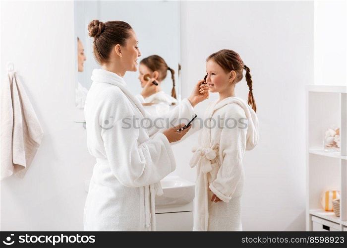 beauty, family and people concept - happy smiling mother and little daughter with brush and powder applying make up in bathroom. mother and daughter applying make up in bathroom