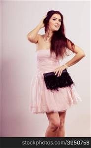 Beauty, fashion and elegant people concept - young brunette slim woman in bright strapless dress holds black clutch bag