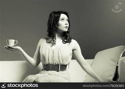 Beauty fashion and relax concept. Fashionable girl holding hot drink coffee or tea cup, sitting on sofa b&amp;w photo