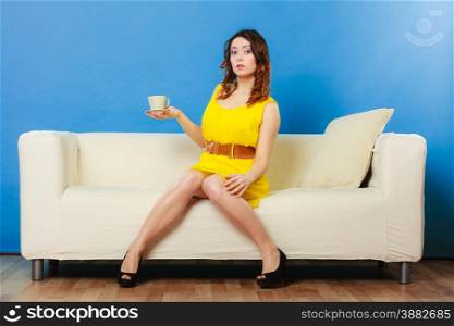 Beauty fashion and relax concept. Fashionable girl yellow dress holding hot drink coffee or tea cup, sitting on sofa