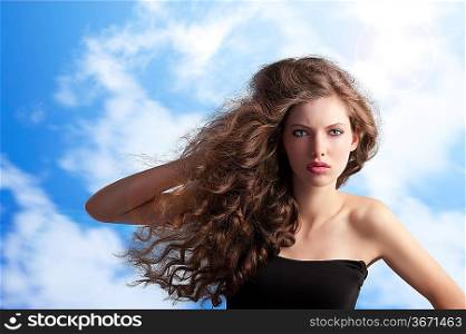 beauty fashion portrait of a very young cute brunette with long curly hair with hairstyle flying in the wind on sky background