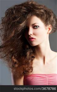 beauty fashion portrait of beautiful young brunette with curly hair flying and creative hairstyle, she looks in to the lens and her face is turned of three-quarters.