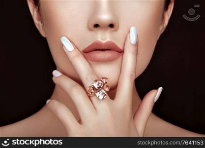 Beauty fashion woman lips with natural Makeup and white nail polish. Gloss brown lipstick. Beauty girl face close up. Sexy lips, manicure, make up. Ring with precious stones, jewelry