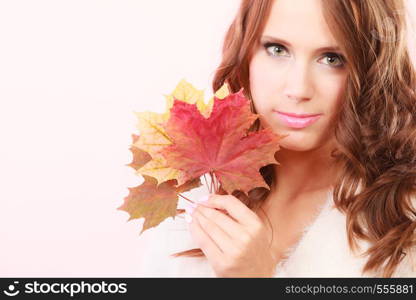 Beauty female autumnal model. Lovely girl long hair with dry fall maple leaves in hand studio shot bright pink background