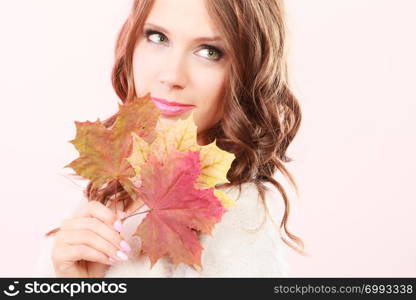 Beauty female autumnal model. Lovely girl long hair with dry fall maple leaves in hand studio shot bright pink background
