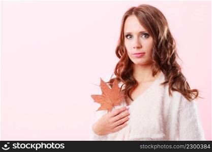 Beauty female autumnal model. Pretty girl long hair wearing warm white sweater with maple leaf in hand