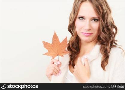 Beauty female autumnal model. Pretty girl long hair wearing warm white sweater with maple leaf in hand