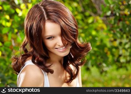 Beauty girl with magnificent curly ringlets against a summer garden