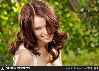 Beauty girl with magnificent curly ringlets against a summer garden