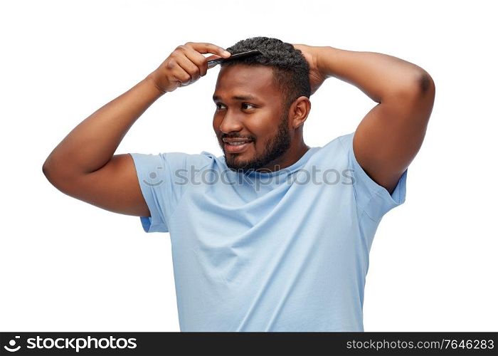 beauty, grooming and hairstyling concept - happy smiling african american man brushing hair with comb over white background. happy african american man brushing hair with comb