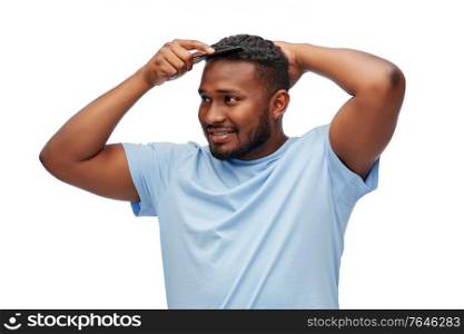 beauty, grooming and hairstyling concept - happy smiling african american man brushing hair with comb over white background. happy african american man brushing hair with comb