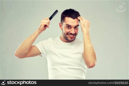 beauty, grooming and people concept - smiling young man brushing hair with comb over gray background. happy man brushing hair with comb over gray