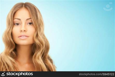 beauty, hair care, people and hairstyle concept - beautiful young woman face with long wavy hair over blue background