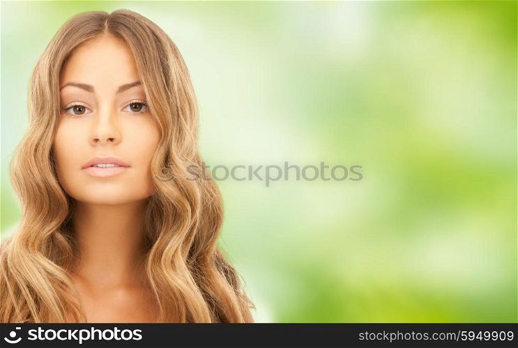 beauty, hair care, people and hairstyle concept - beautiful young woman face with long wavy hair over green natural background