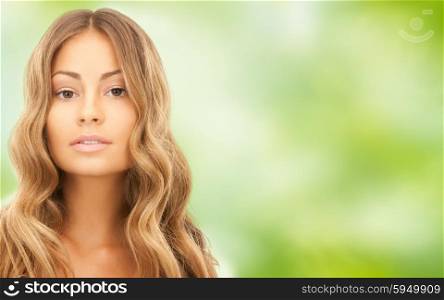 beauty, hair care, people and hairstyle concept - beautiful young woman face with long wavy hair over green natural background