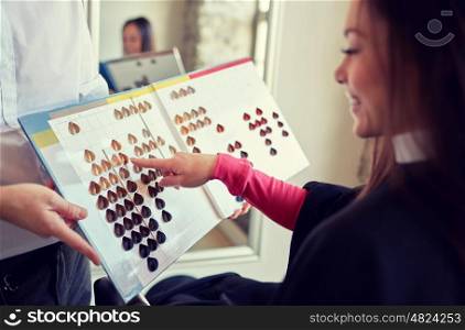 beauty, hair dyeing and people concept - happy young woman with hairdresser choosing hair color from palette samples at salon